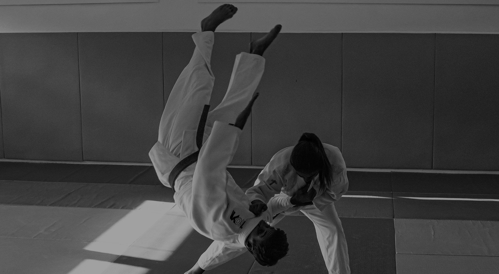 Deux judokas en kimono blanc sur le tatami, l'un projetant l'autre